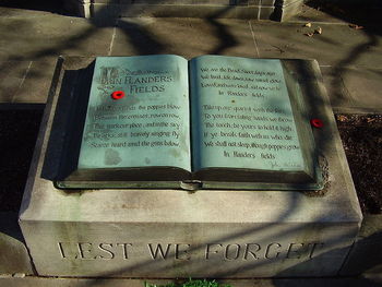 Remembrance Day at the John McCrae House (birthplace, museum, & memorial) in Guelph, Ontario Canada. A detail shot of the "altar" of the memorial, with the complete poem "In Flander's Fields" & the line "LEST WE FORGET" inscribed on it. 2 Canadian remembrance day poppy pins & part of a wreath are visible. Image source: Wikipedia